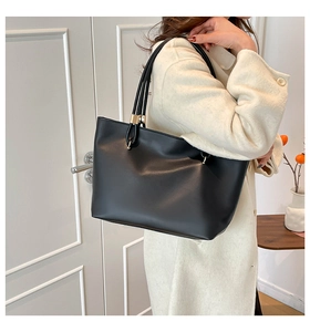 Detail of a matte black tote bag with gold metal hardware on a beige wool coat