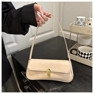Close-up of beige patent leather baguette bag with a gold oval metal lock and sleek strap
