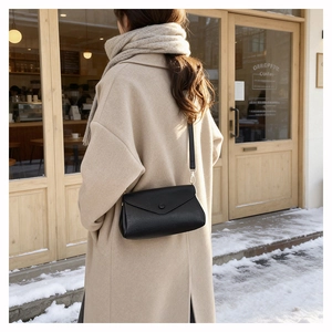 Detail of a black leather envelope bag styled with a beige wool coat in a snowy setting