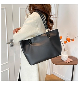 Close-up of minimalist black leather tote bag worn on shoulder in a cozy home setting