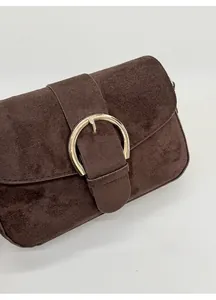 Detail of dark brown suede shoulder bag featuring a large decorative gold round buckle
