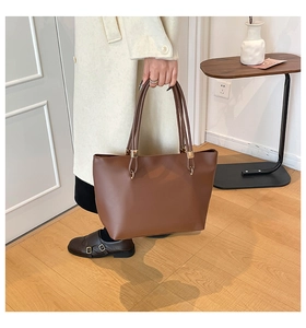 Detail of dark brown leather tote bag with gold hardware held by model in beige coat