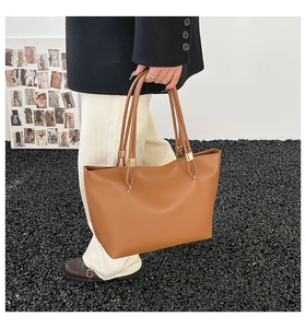 Brown tote bag with gold metal accents shown on a model in a minimalist setting