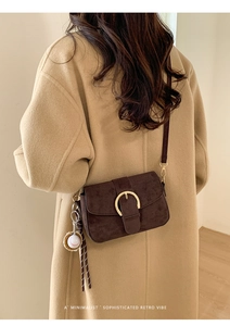 Detail of retro brown suede shoulder bag with gold metal buckle and baseball charm accessory