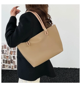 Detail of light khaki tote bag featuring slim handles and elegant gold metal buckles
