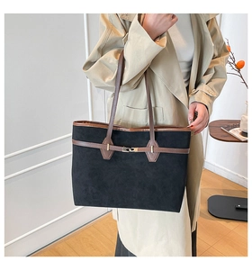 Détail d'un grand cabas en daim noir avec anses en cuir marron porté avec un trench beige