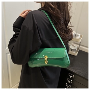 Detail of green patent leather baguette bag with curved gold buckle in lifestyle setting