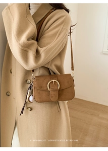 Detail of caramel suede crossbody bag with gold round buckle and baseball charm
