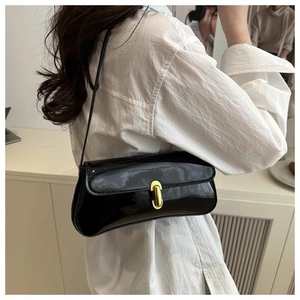 Detail of black patent leather underarm bag with gold oval clasp on white shirt