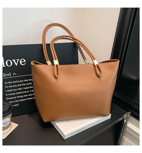 Detail of brown faux leather tote bag showing slim handles and golden hardware accents