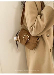 Close-up of brown suede shoulder bag with gold buckle and creative baseball pendant charm