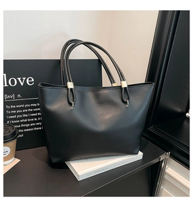 Close-up of black leather tote bag with gold metal handle accents on a modern table