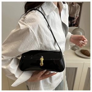 Detail of a shiny black patent leather underarm bag featuring a bold gold buckle closure
