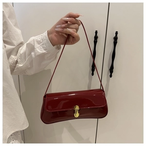 Detailed close-up of glossy deep red lacquer underarm bag with gold metal buckle closure