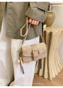 Detail der beigen Wildleder-Umhängetasche mit goldener Ringschnalle und Baseball-Schlüsselanhänger