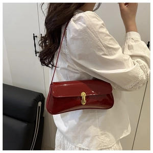 Detail of red patent leather underarm bag with gold metal clasp on a model