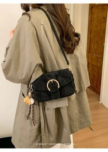 Detail of a minimalist black suede shoulder bag featuring a prominent gold round buckle closure