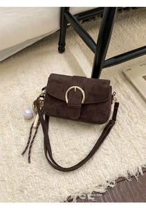 Detail of dark brown suede shoulder bag with gold buckle and baseball charm on a plush rug