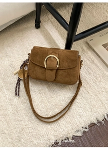 Detail of retro brown suede shoulder bag featuring a gold round buckle and textured charm
