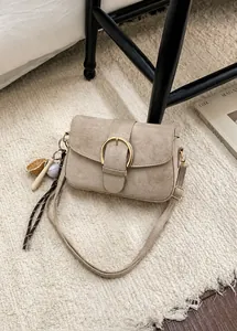 Detalle de bolso bandolera de ante beige con hebilla dorada y colgantes de béisbol