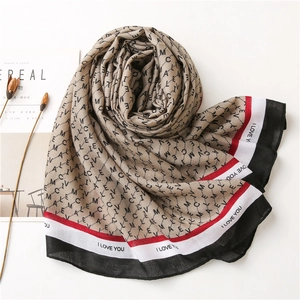 Détail d'un foulard en soie kaki avec imprimés de lettres et bordures rayées rouges