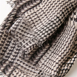 Dettaglio macro di motivi pied-de-poule e geometrici su un morbido foulard con frange