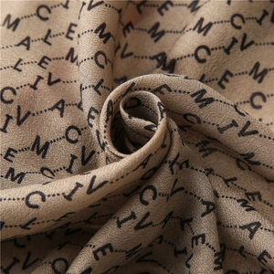 Gros plan d'un foulard kaki montrant l'imprimé lettres et la texture tissée douce