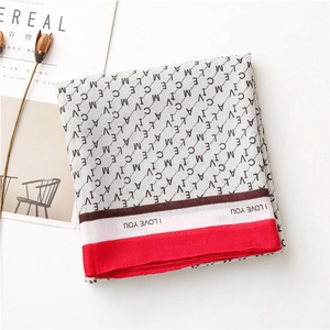 Détail d'un foulard en soie beige avec lettres noires et bordures rayées rouges