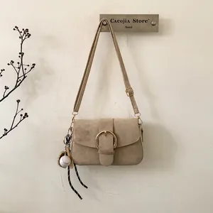 Beige suede flap shoulder bag with gold hardware and baseball glove charm on wall