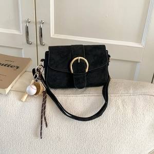 Matte black suede shoulder bag with gold round buckle and sports charms on a soft sofa