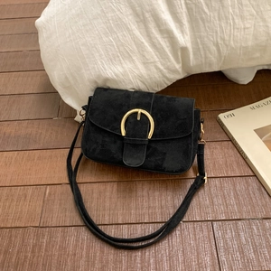 Detail of black suede shoulder bag featuring a prominent gold semicircular buckle closure