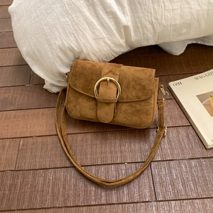 Brown suede crossbody bag with golden metal buckle on wooden floor with accessories