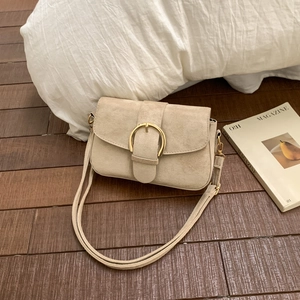 Close-up of beige suede handbag with gold buckle on wooden floor and white pillow