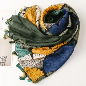 Detail of artistic ginkgo leaf print scarf with colorful tassel fringes on light fabric