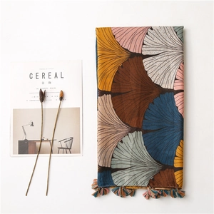 Detail of artistic ginkgo leaf print scarf with colorful woven fringe tassels on white background