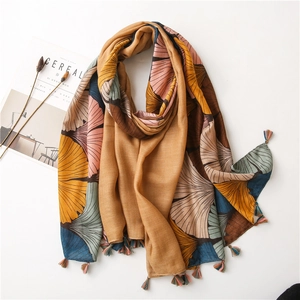 Close-up of artistic ginkgo leaf print shawl with colorful fringe tassels on white surface