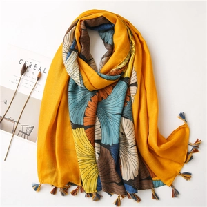 Detail of yellow ginkgo leaf print scarf with colorful fringe on a neutral background