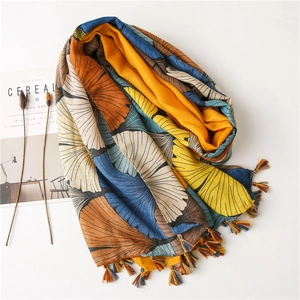 Detail of artistic ginkgo leaf print scarf with multi-color tassels on white background