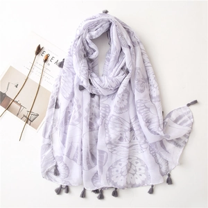 Gros plan d'une écharpe à motifs papillons en tissu lilas avec d'élégants pompons gris