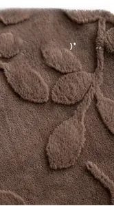 Detail of dark brown tufted plush fabric showing leaf pattern texture and soft fibers