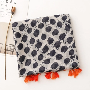 Détail d'une écharpe en coton et lin avec pois noirs et glands orange vif aux bords