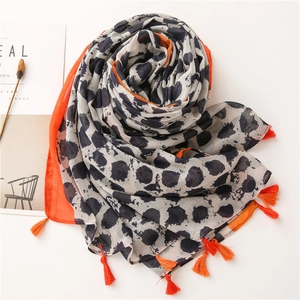 Détail d'une écharpe à motif léopard bleu avec bordure orange et pompons assortis