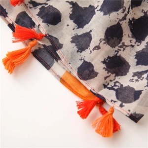 Détail macro d'une écharpe en coton et lin avec imprimé bleu et pompons orange vifs