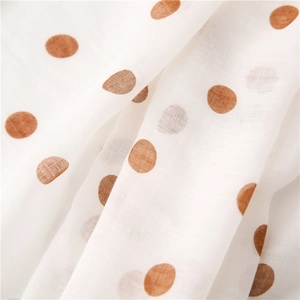 Detailed close-up of soft cotton linen fabric featuring large brown polka dots on white