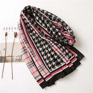 Detailed view of pink and black houndstooth cotton scarf with fringed edges on a magazine