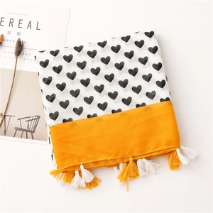 Detail of white cotton scarf with black hearts, yellow hem, and fringe tassels