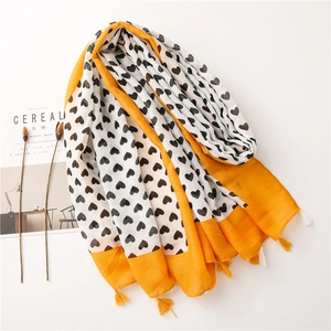 Detail of linen scarf with heart print, yellow borders and tassel fringe on white background
