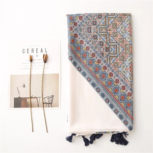 Détail d'une écharpe en coton et lin avec motifs géométriques et pompons bleus au bord