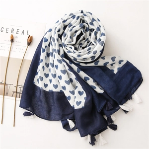 Detail of navy blue heart print scarf with decorative tassel edges on a white surface