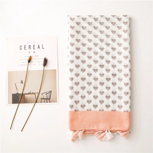 Detail of white cotton linen scarf featuring grey heart prints and pink tassel fringe